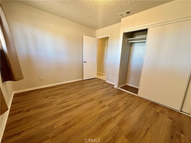 unfurnished bedroom with wood-type flooring, a textured ceiling, and a closet