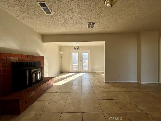 unfurnished living room with french doors, a textured ceiling, light tile patterned floors, an inviting chandelier, and a wood stove