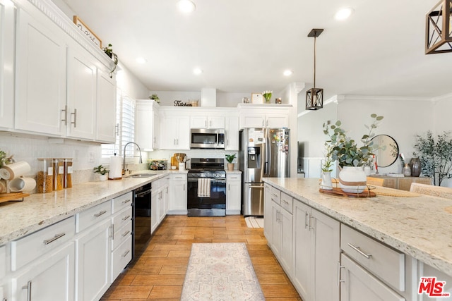 kitchen featuring appliances with stainless steel finishes, ornamental molding, sink, decorative light fixtures, and white cabinetry