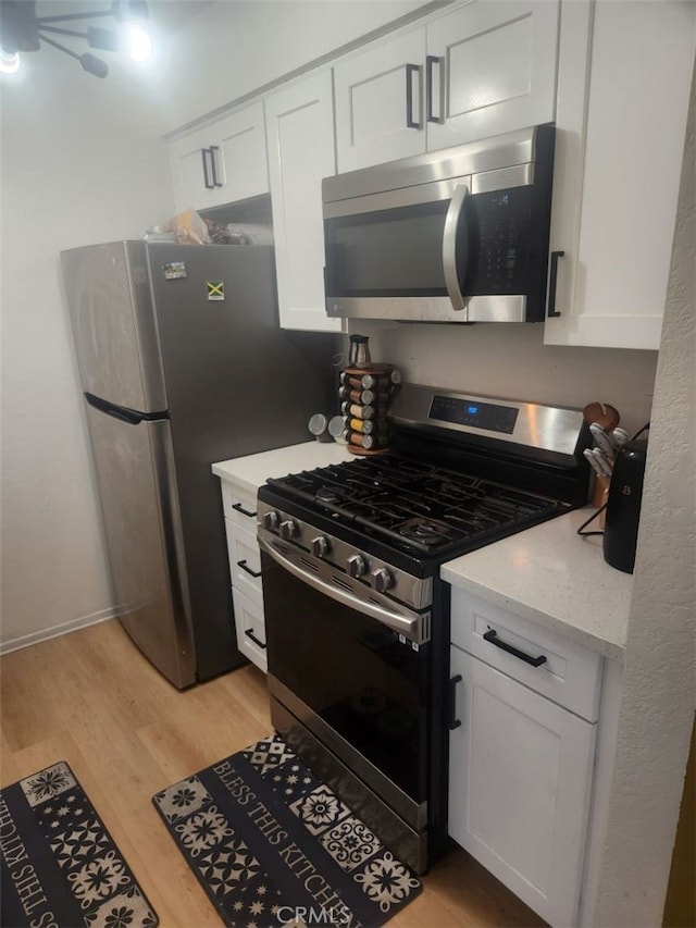 kitchen with light stone countertops, white cabinetry, stainless steel appliances, and light hardwood / wood-style flooring