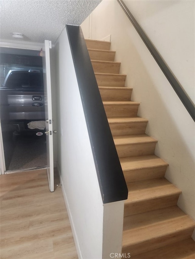 staircase featuring a textured ceiling and hardwood / wood-style flooring