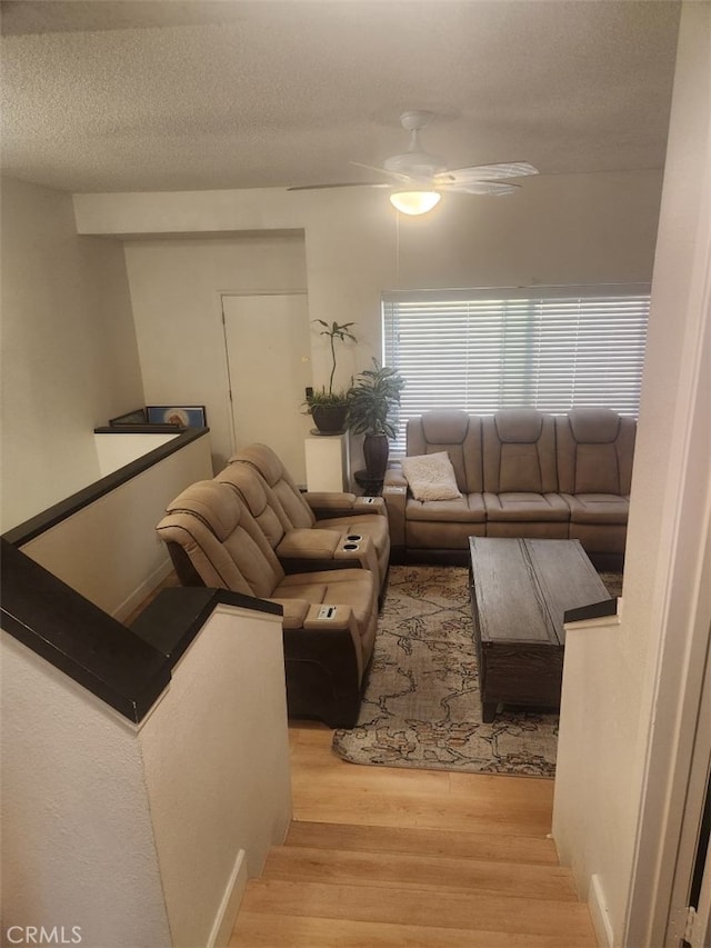 living room featuring ceiling fan, light hardwood / wood-style floors, and a textured ceiling