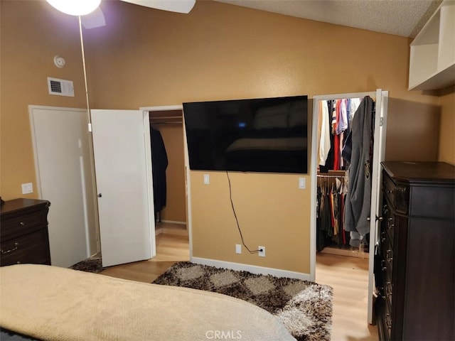 bedroom with ceiling fan, light hardwood / wood-style floors, a textured ceiling, and a closet