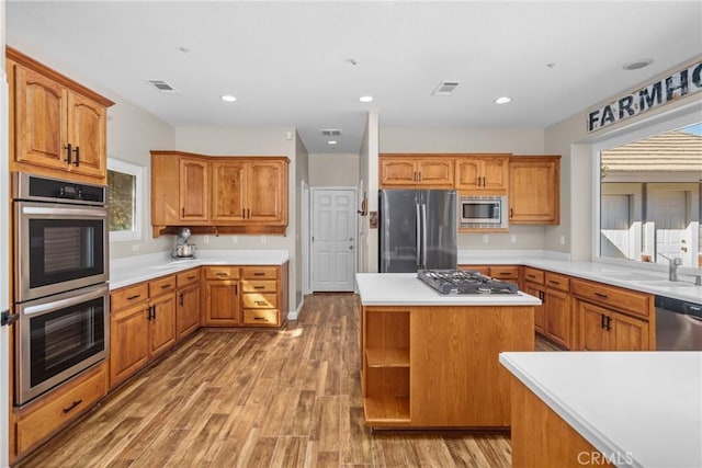 kitchen with sink, a kitchen island, wood-type flooring, and appliances with stainless steel finishes