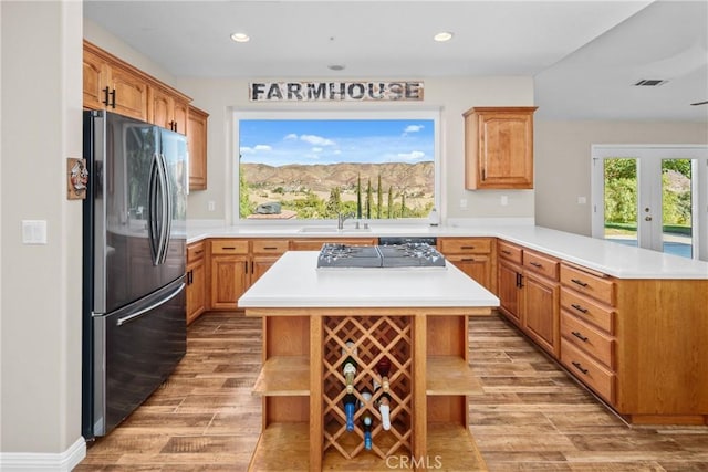 kitchen with kitchen peninsula, a kitchen bar, refrigerator, black gas stovetop, and light hardwood / wood-style floors