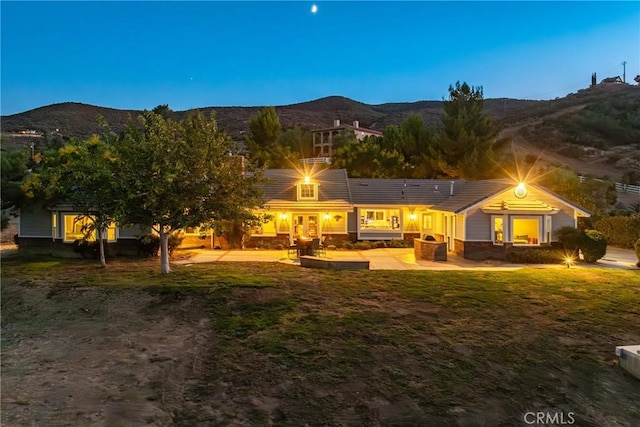 back house at dusk featuring a lawn, a mountain view, and a patio area