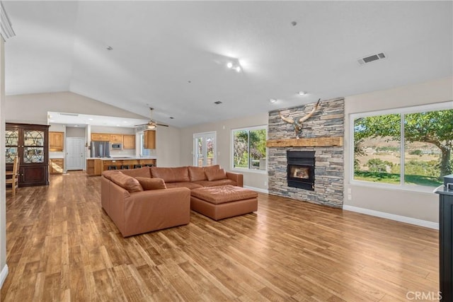 living room featuring light hardwood / wood-style flooring, ceiling fan, lofted ceiling, and a stone fireplace