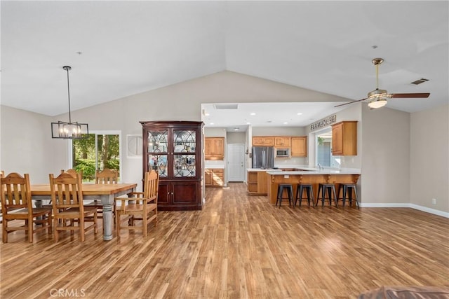 dining space with ceiling fan with notable chandelier, vaulted ceiling, and light hardwood / wood-style flooring