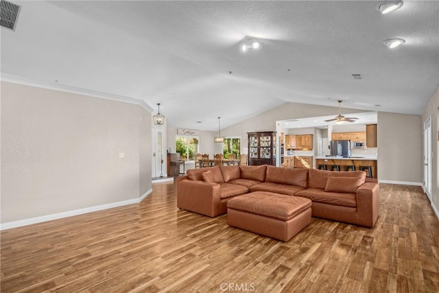 living room with a textured ceiling, lofted ceiling, light wood-type flooring, and crown molding