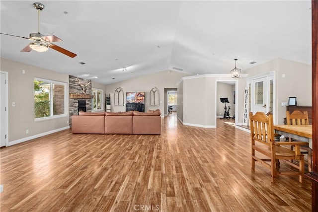 living room featuring a stone fireplace, light hardwood / wood-style flooring, ceiling fan with notable chandelier, and vaulted ceiling