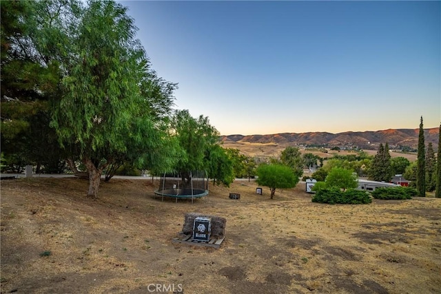 yard at dusk featuring a mountain view and a trampoline