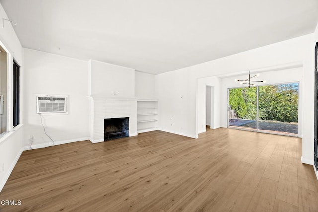 unfurnished living room with an inviting chandelier, wood-type flooring, a fireplace, and an AC wall unit