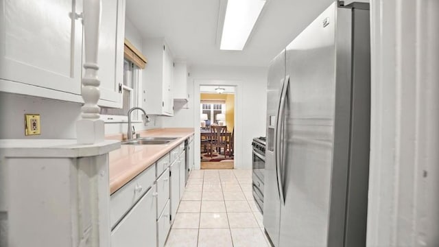 kitchen with light tile patterned floors, stainless steel appliances, white cabinetry, and sink