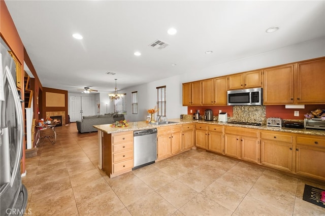 kitchen featuring stainless steel appliances, light stone counters, kitchen peninsula, pendant lighting, and ceiling fan with notable chandelier