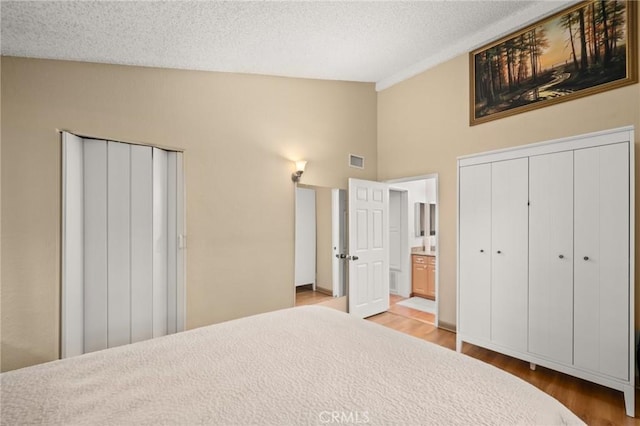 bedroom with a textured ceiling, connected bathroom, two closets, and hardwood / wood-style flooring