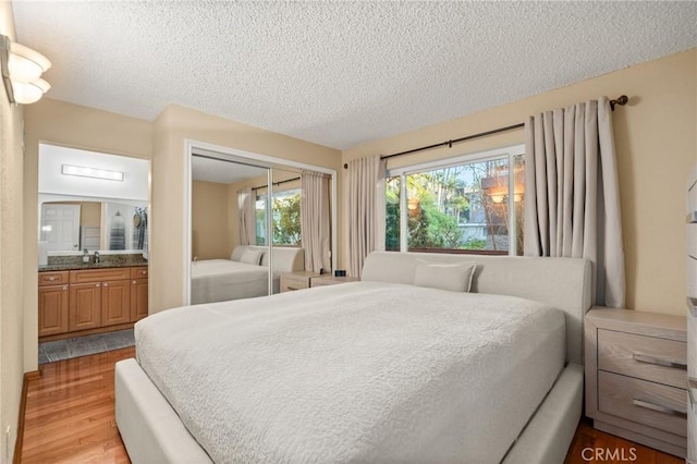 bedroom featuring a textured ceiling, light wood-type flooring, a closet, and connected bathroom