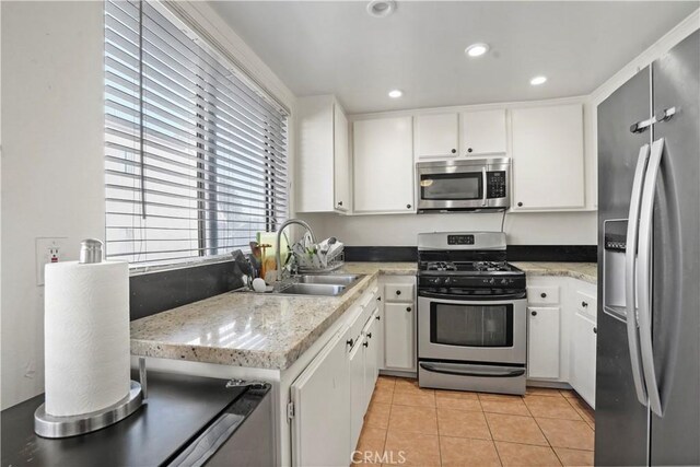 kitchen featuring light stone countertops, white cabinets, appliances with stainless steel finishes, sink, and light tile patterned floors