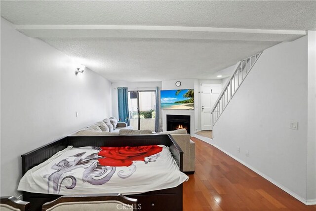 bedroom with a textured ceiling, hardwood / wood-style flooring, and beamed ceiling