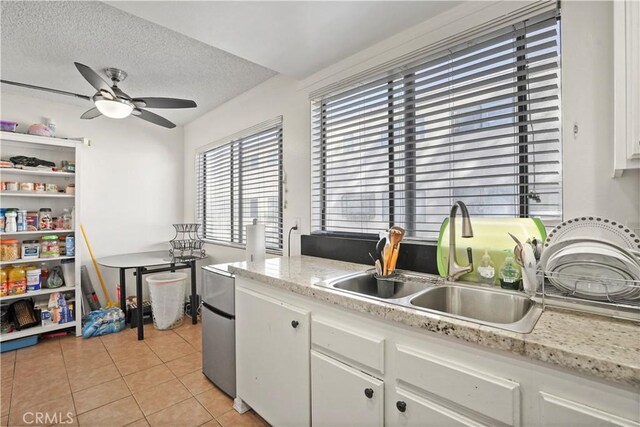 kitchen with sink, white cabinetry, light stone countertops, a textured ceiling, and light tile patterned floors