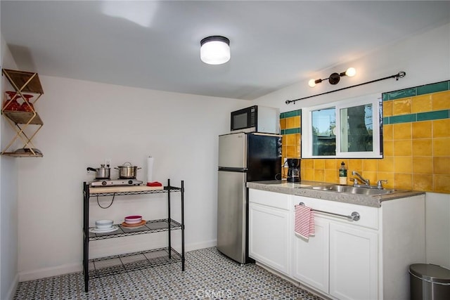 kitchen featuring white cabinets, decorative backsplash, stainless steel refrigerator, and sink