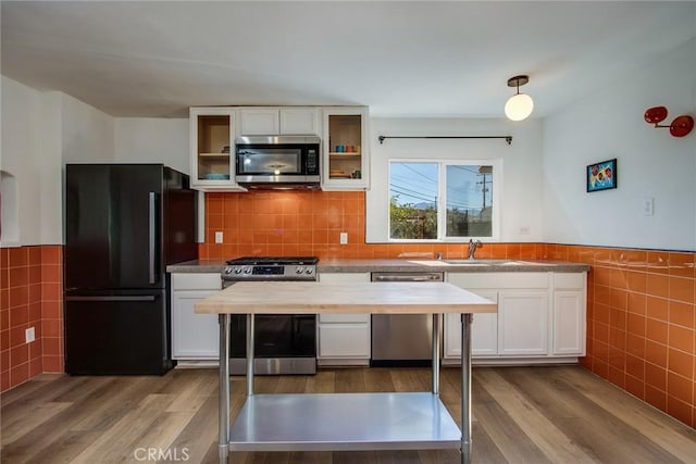 kitchen with white cabinetry, hardwood / wood-style floors, stainless steel appliances, and tile walls