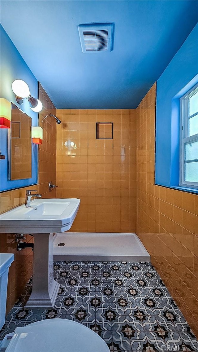 bathroom featuring tile patterned flooring, a tile shower, toilet, and tile walls