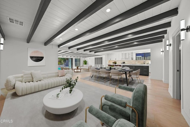 living room featuring beam ceiling, light hardwood / wood-style flooring, and sink