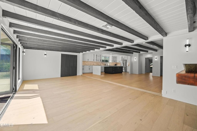 unfurnished living room featuring beam ceiling, sink, and light hardwood / wood-style floors