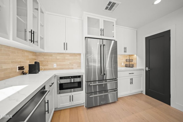 kitchen featuring light stone countertops, stainless steel appliances, light hardwood / wood-style flooring, backsplash, and white cabinets