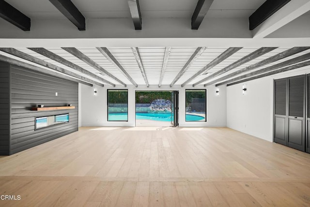 unfurnished living room with beamed ceiling and light wood-type flooring