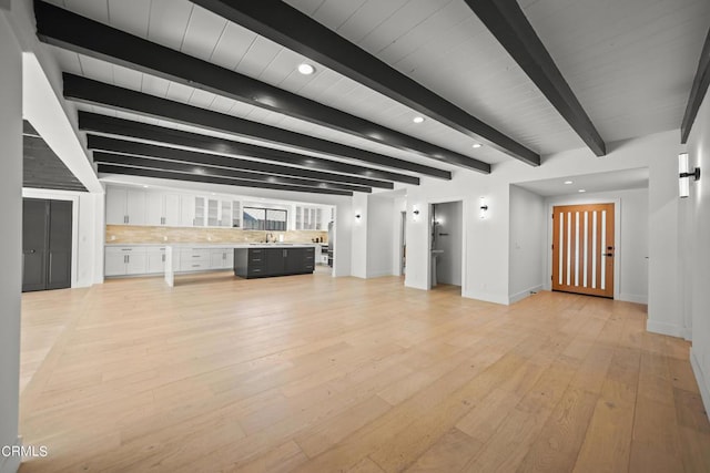 unfurnished living room with light hardwood / wood-style floors, sink, and beam ceiling