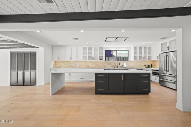 kitchen with beamed ceiling, stainless steel appliances, white cabinetry, and a center island with sink