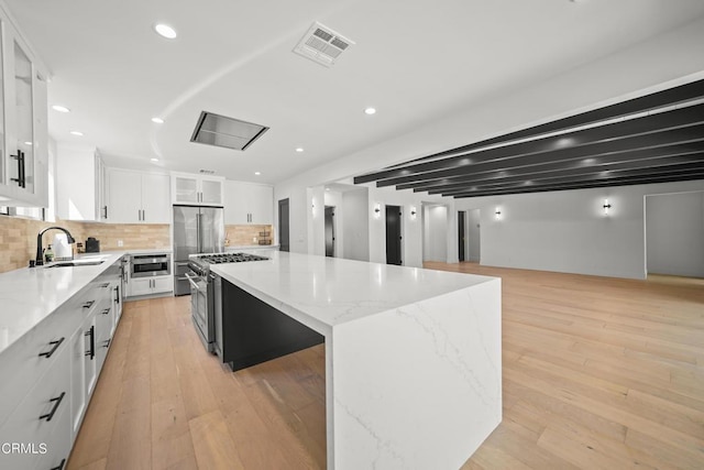 kitchen with a spacious island, white cabinetry, stainless steel appliances, and light hardwood / wood-style flooring