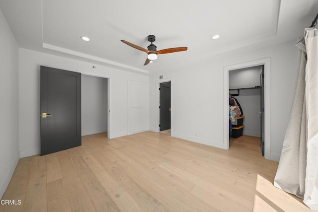 unfurnished bedroom featuring a raised ceiling, ceiling fan, a spacious closet, light hardwood / wood-style floors, and a closet