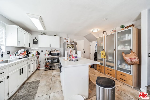 kitchen featuring stainless steel appliances, sink, light tile patterned floors, white cabinets, and a kitchen island