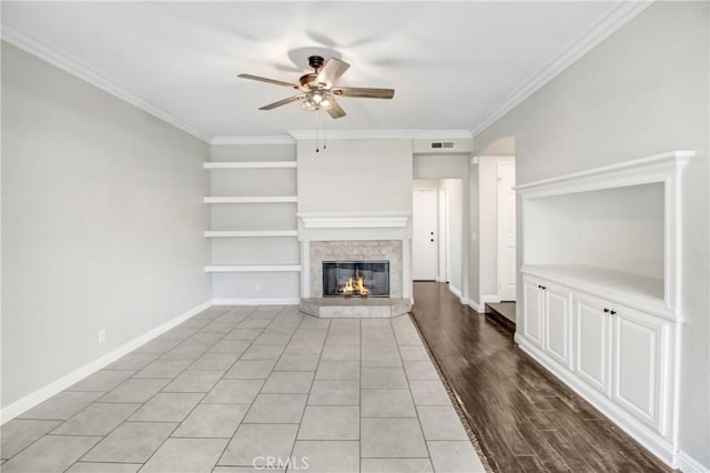 unfurnished living room featuring built in shelves, light hardwood / wood-style floors, ceiling fan, and crown molding