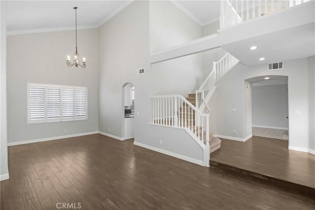 unfurnished living room with a chandelier, a high ceiling, dark hardwood / wood-style floors, and ornamental molding