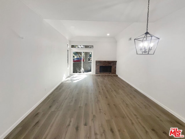 unfurnished living room with an inviting chandelier, dark hardwood / wood-style floors, and a brick fireplace