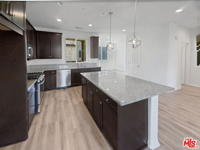 kitchen with pendant lighting, light hardwood / wood-style flooring, a kitchen island, light stone counters, and stainless steel appliances