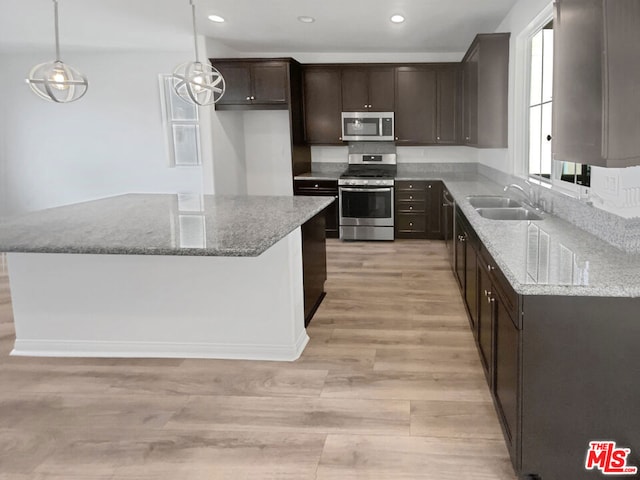 kitchen featuring sink, light stone countertops, appliances with stainless steel finishes, decorative light fixtures, and light hardwood / wood-style floors