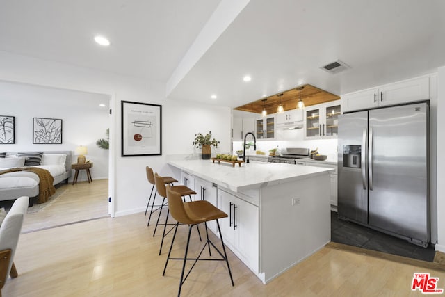 kitchen with light hardwood / wood-style floors, stove, stainless steel refrigerator with ice dispenser, a kitchen bar, and white cabinetry