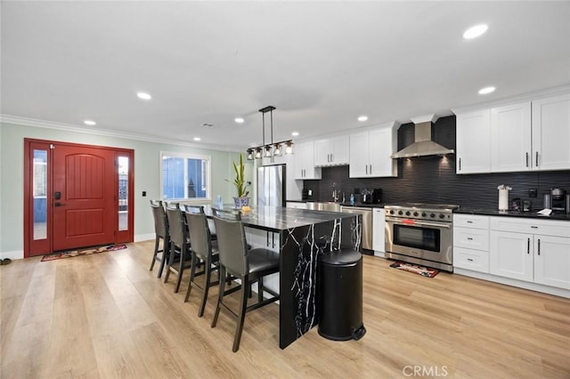 kitchen featuring wall chimney range hood, light hardwood / wood-style flooring, pendant lighting, a kitchen island, and appliances with stainless steel finishes