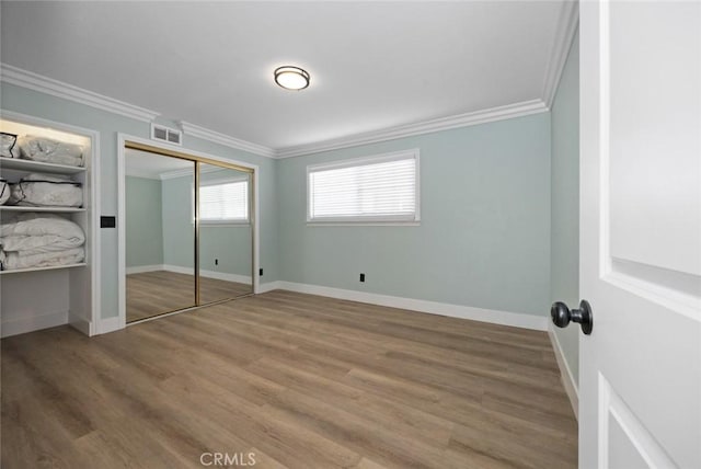 unfurnished bedroom with wood-type flooring, a closet, and crown molding