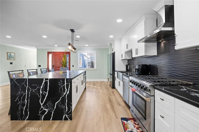 kitchen featuring a center island, stainless steel appliances, wall chimney range hood, light hardwood / wood-style flooring, and pendant lighting