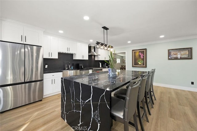 kitchen featuring a center island, hanging light fixtures, stainless steel appliances, wall chimney range hood, and light hardwood / wood-style flooring