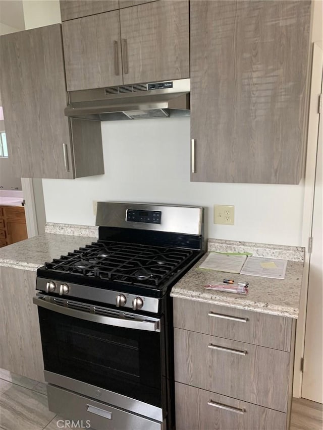 kitchen with light stone counters, extractor fan, light wood-type flooring, and stainless steel range with gas stovetop