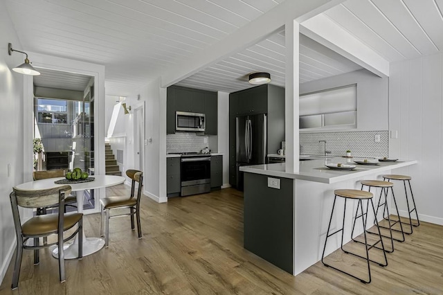 kitchen featuring appliances with stainless steel finishes, a kitchen bar, decorative backsplash, light hardwood / wood-style floors, and kitchen peninsula