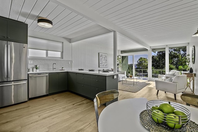 kitchen with appliances with stainless steel finishes, sink, backsplash, kitchen peninsula, and light wood-type flooring