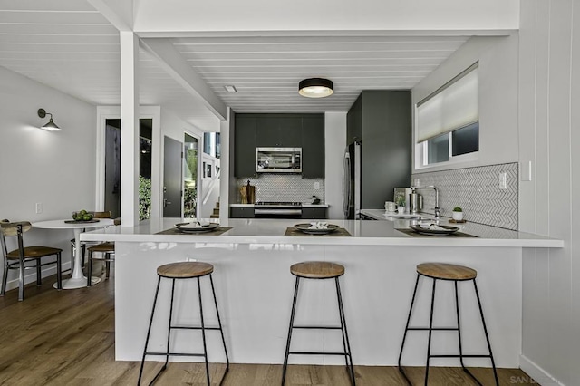 kitchen with kitchen peninsula, a breakfast bar area, appliances with stainless steel finishes, backsplash, and sink