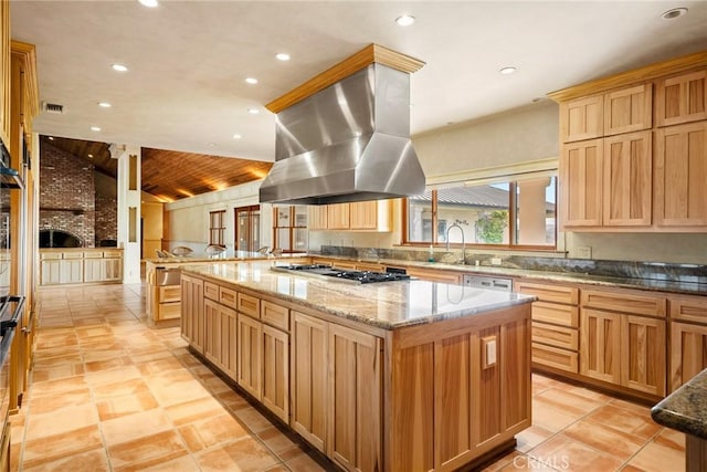 kitchen featuring a brick fireplace, light stone counters, island range hood, stainless steel gas stovetop, and a large island